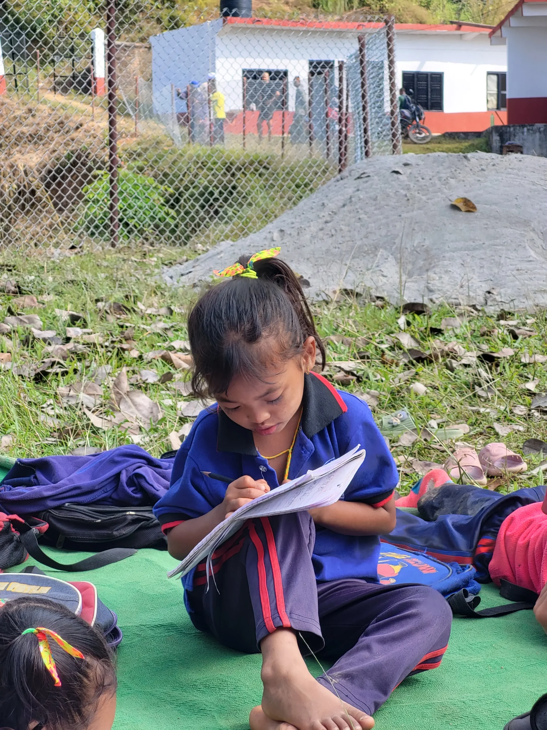 Élève qui étudie assise par terre devant l’école rénovée.